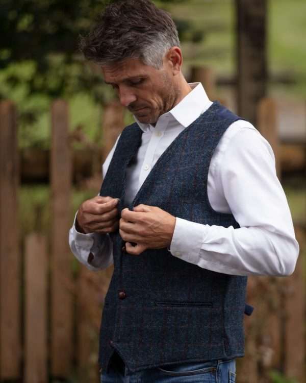 1T1A9997 scaled 1 These world famous Harris Tweed Waistcoats are superbly tailored, hard wearing and warm. When purchasing one of these waistcoats you are guaranteed exceptional quality. By law Harris Tweed must come from the Outer Hebrides, and be hand woven from local wool. Supplied by Harris Tweed Scotland from 100% pure virgin wool, dyed, spun and finished in the Western Isles of Scotland. Hand-woven by crofters in their own homes on the islands of Lewis, Harris, Uist and Barra. Hand finished to the highest standard with four leather button fastening. Other specifications include two welter outer ticket pockets, Fully lined and Satin back lining with adjustable strap and buckle . Spare Leather Button included. Dress with matching Blazer for an extremely stylish look perfect for weddings and the races. All our tweeds are stamped with the authentic, official gold crossed orb mark of the Harris Tweed Authority.