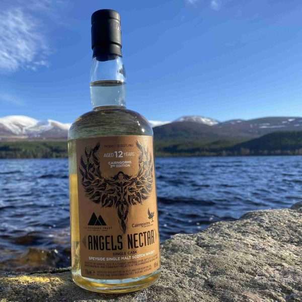 A bottle of Angels' Nectar Cairngorms 3rd Edition beside Loch Morlich